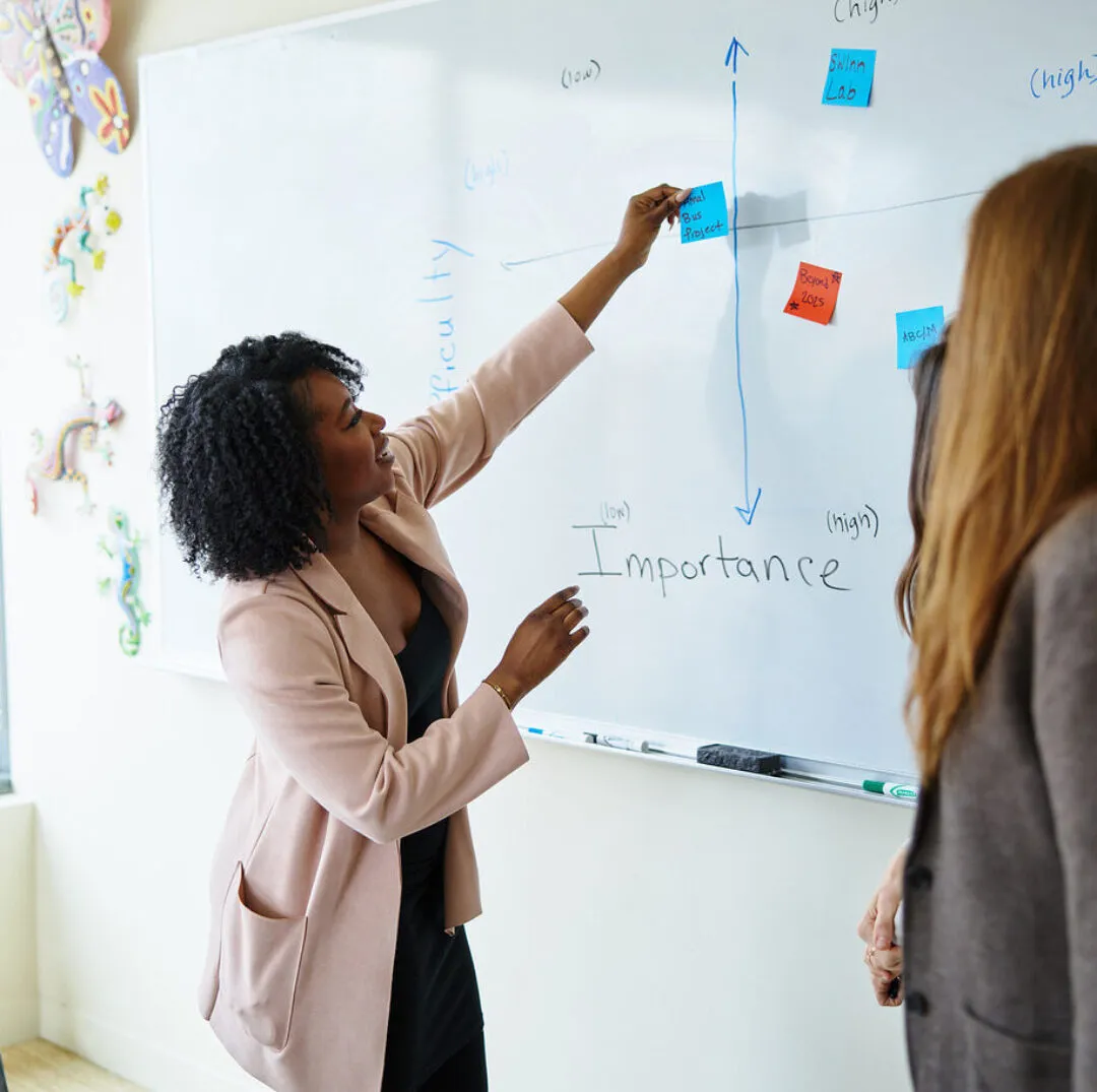 A CISWH team member leads a discussion at a whiteboard, placing sticky notes on a graph while engaging with another participant.