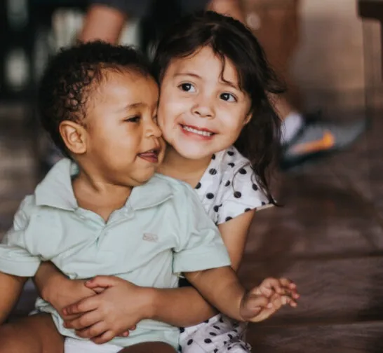 two children sit on floor hugging