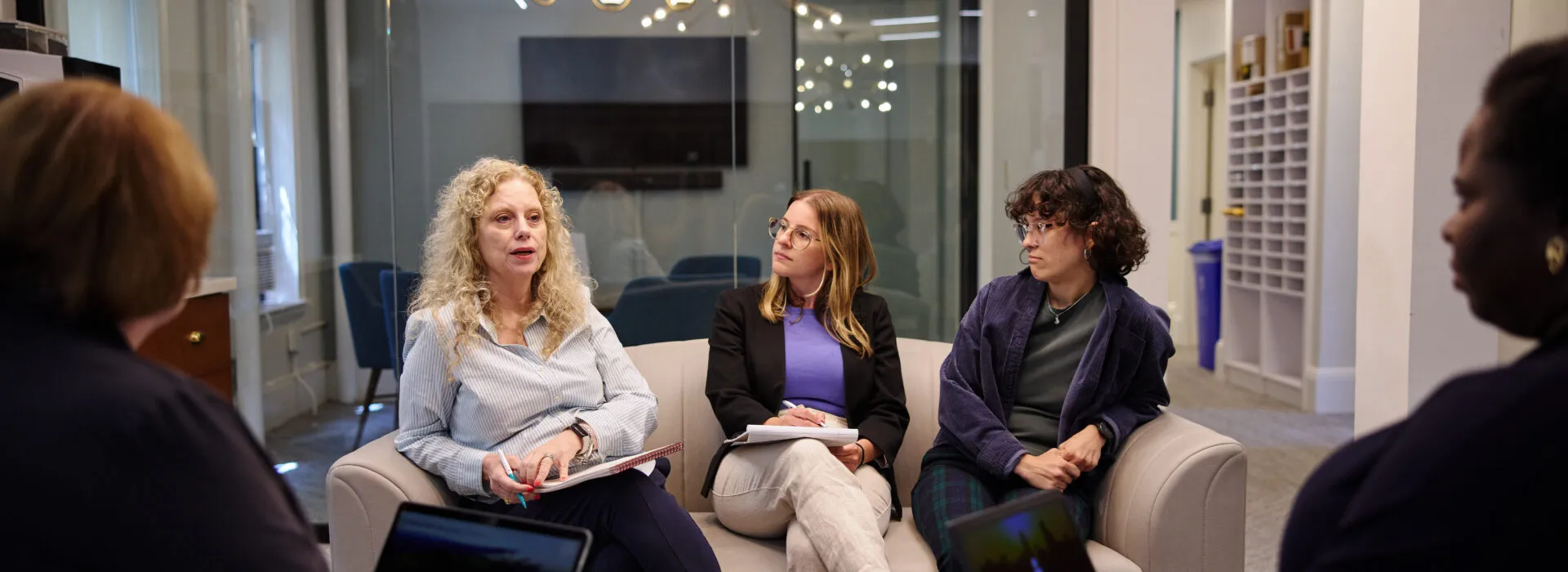 CISWH team members sit in a circle during a collaborative meeting in a modern office space, actively engaged in discussion with laptops and notebooks.