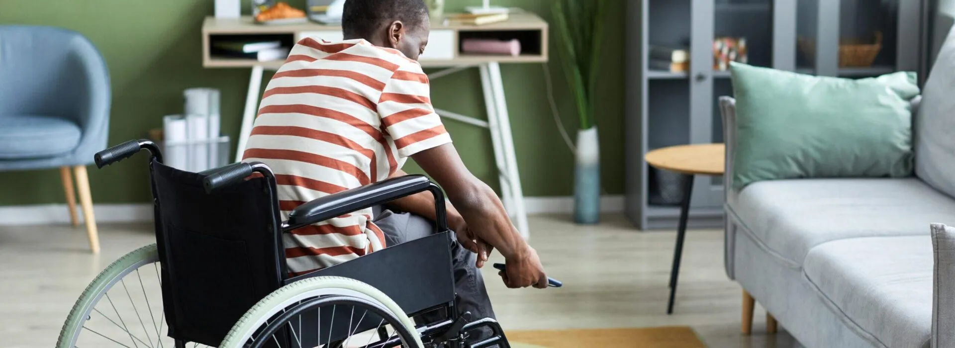 A young person in a wheelchair moves through a brightly lit, modern living room with a romote in their hand.