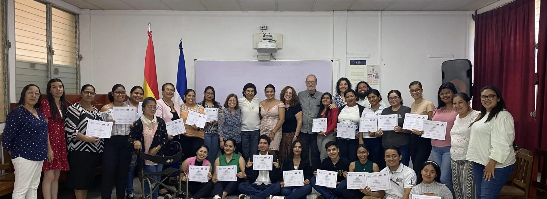 A large group of people pose indoors for a photo, many holding certificates, after an event.